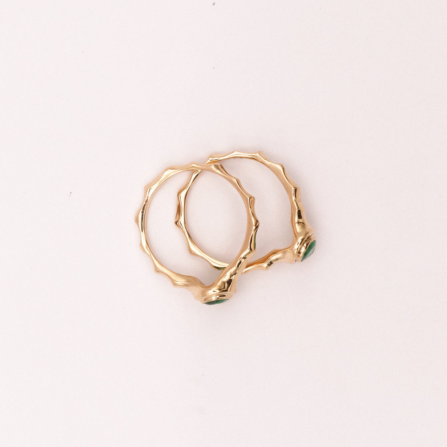 Gold ring with a green gemstone on a light pink background