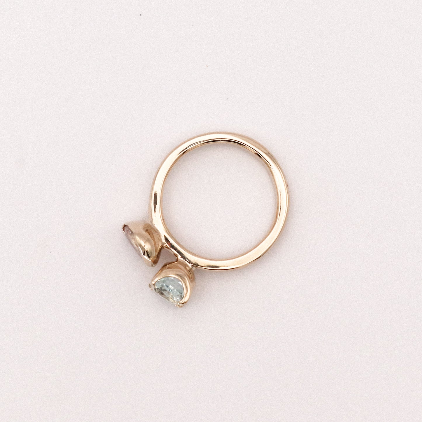 Gold ring with two gemstones on a light pink background