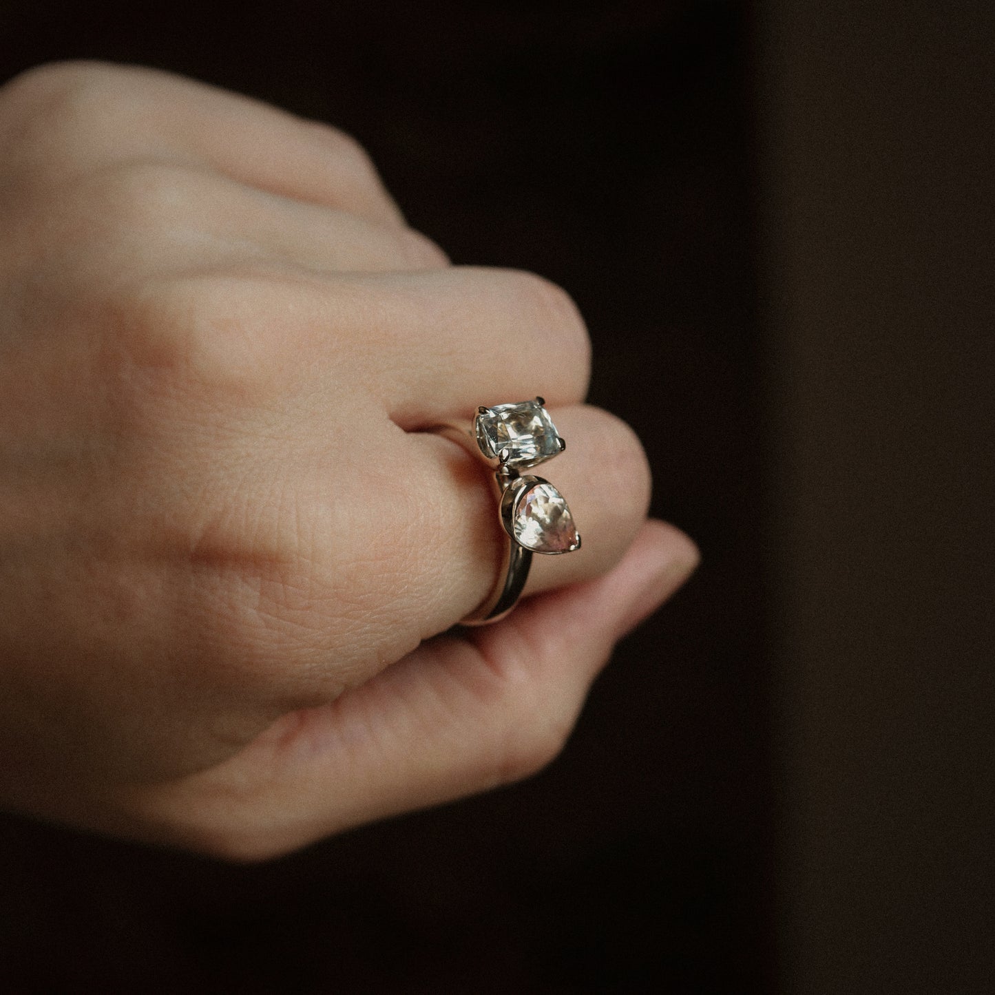Close-up of a hand wearing a silver ring with a diamond on a dark background
