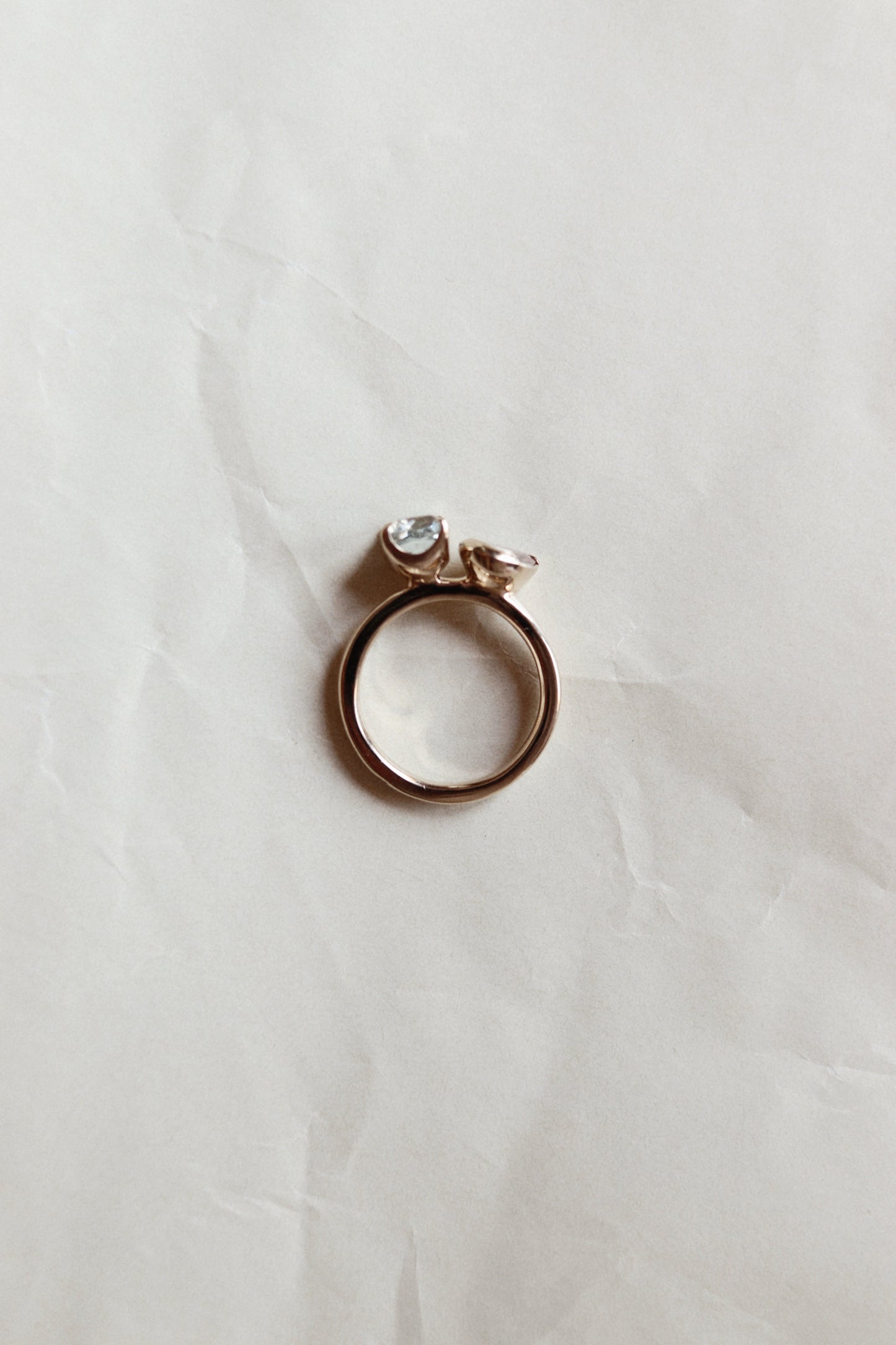 A rose gold ring with a small clear gemstone, resting on a wrinkled white paper background.