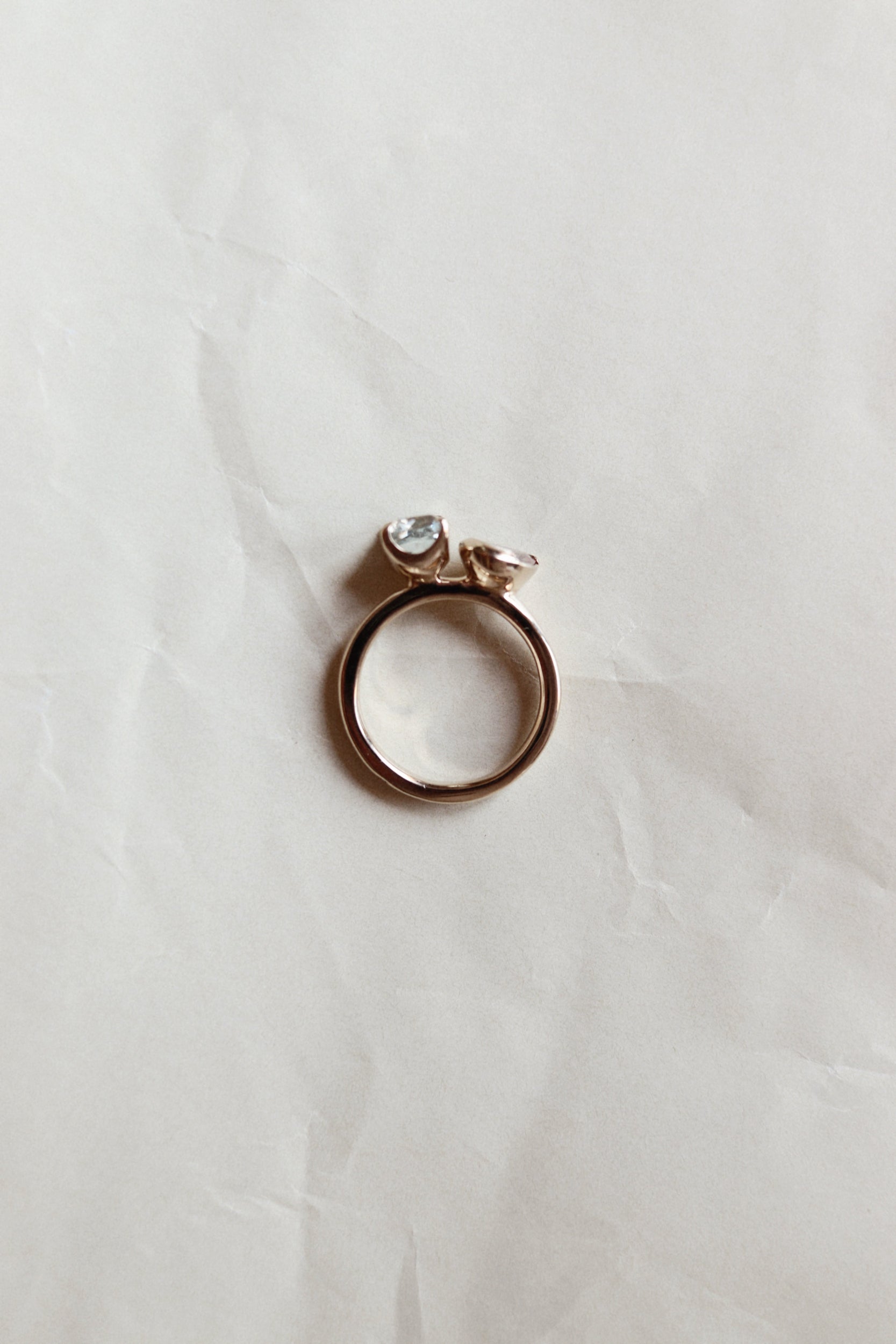 A rose gold ring with a small clear gemstone, resting on a wrinkled white paper background.