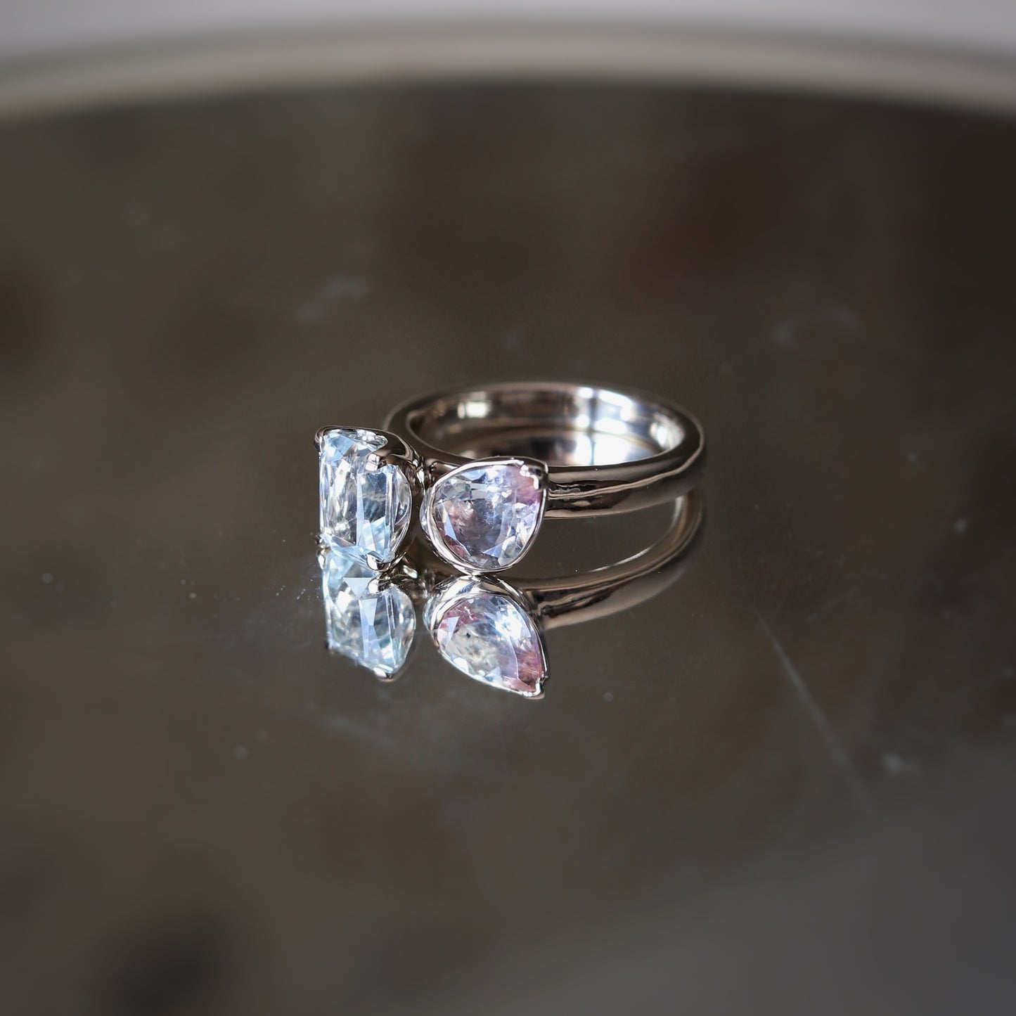 Silver ring with three clear gemstones on a reflective surface