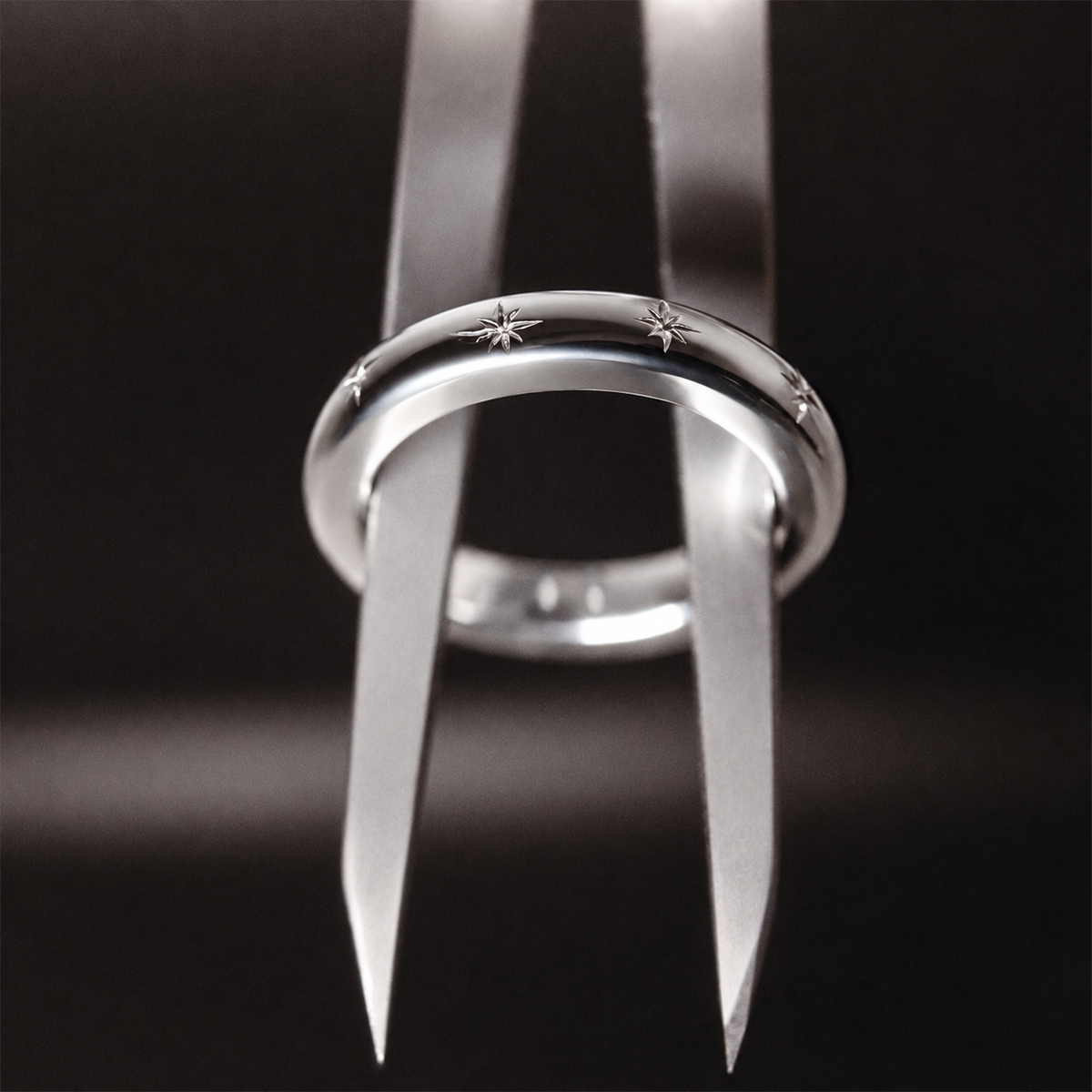 A polished silver-toned ring with engraved star motifs, shown in close-up against a dark black background.