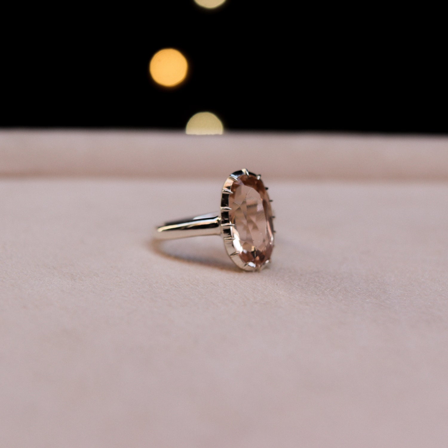 Silver ring with a large gemstone on a pink surface with blurred lights in the background