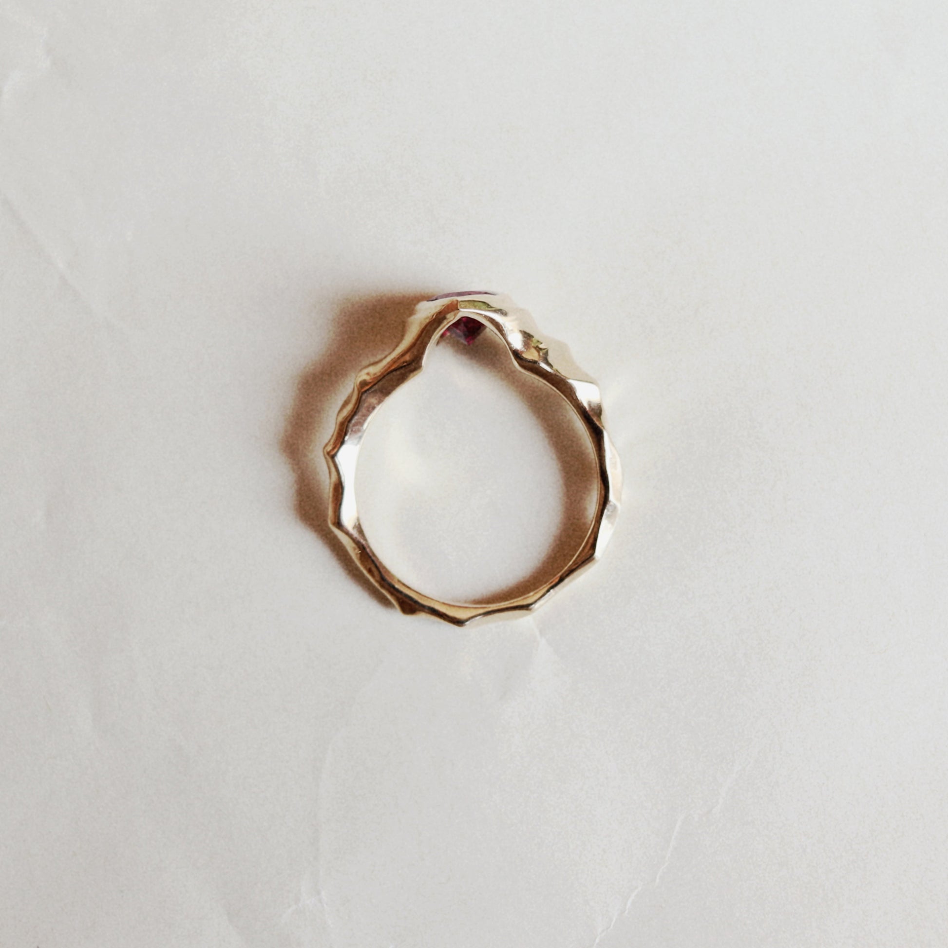 A textured, organic-shaped gold ring lying on a light beige, slightly wrinkled paper background.