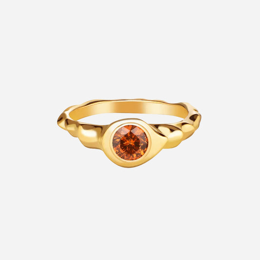 A round cut orange garnet stone set in a gold ring with a polished finish.