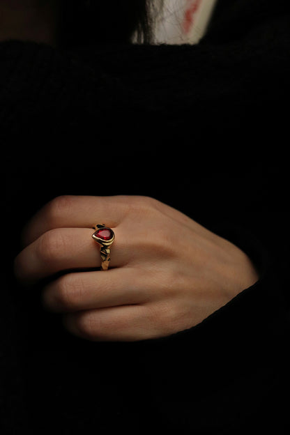 Hand wearing a gold ring with a red stone on a dark background