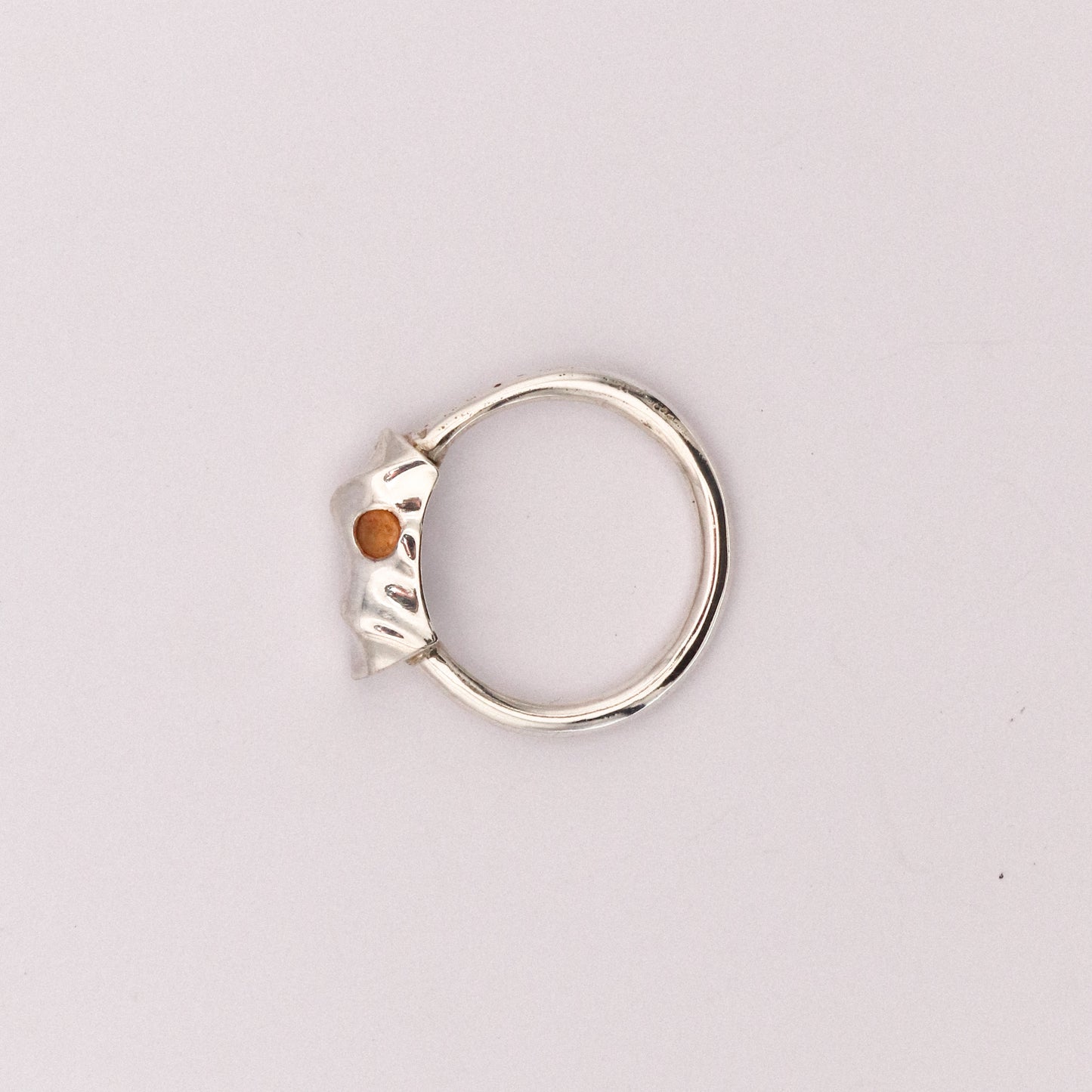 Silver ring with a small orange stone on a light gray background