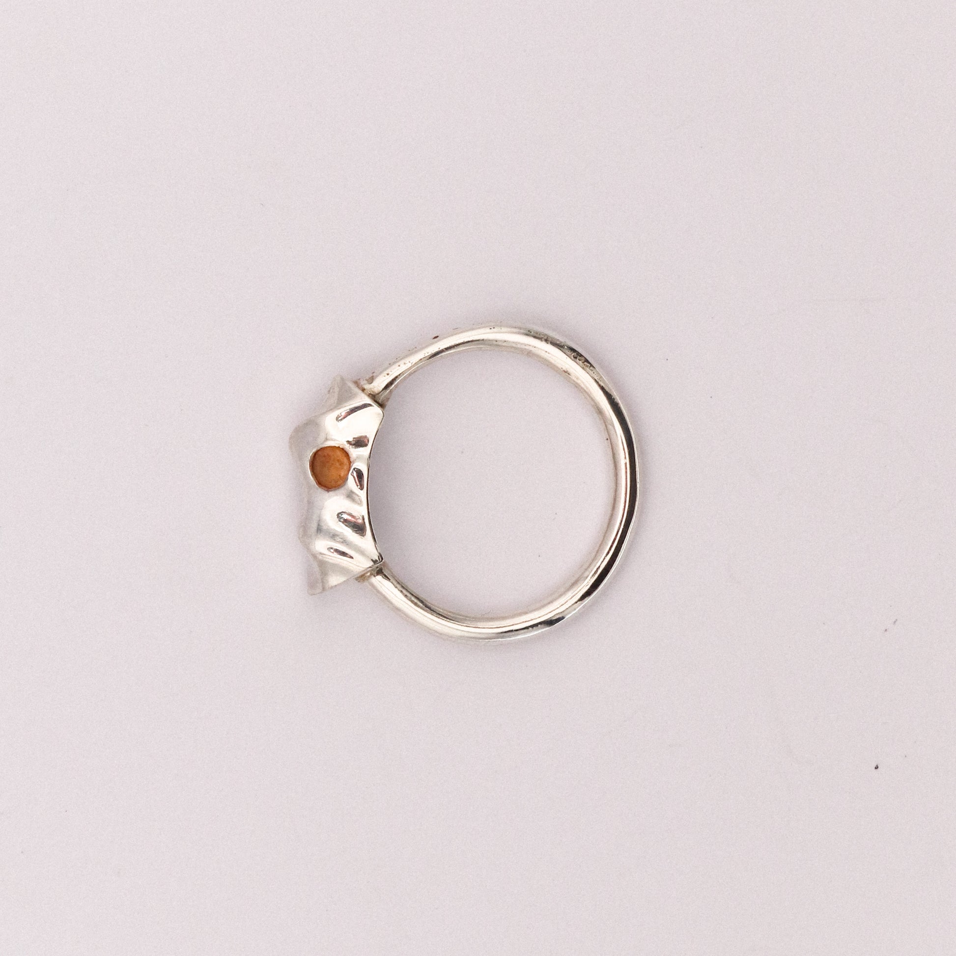 Silver ring with a small orange stone on a light gray background