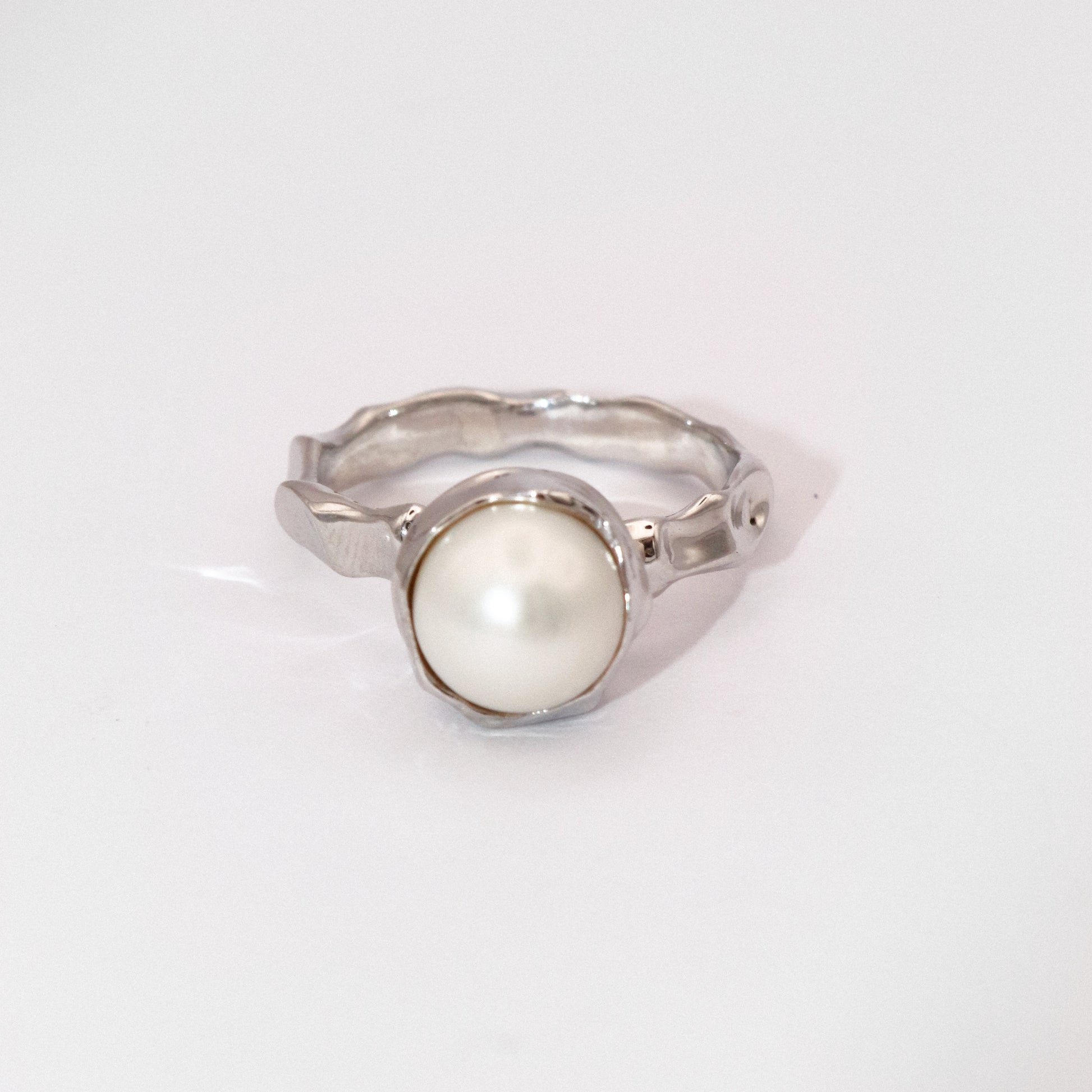 Silver ring with a white pearl on a light gray background
