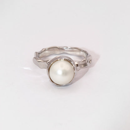 Silver ring with a white pearl on a light gray background