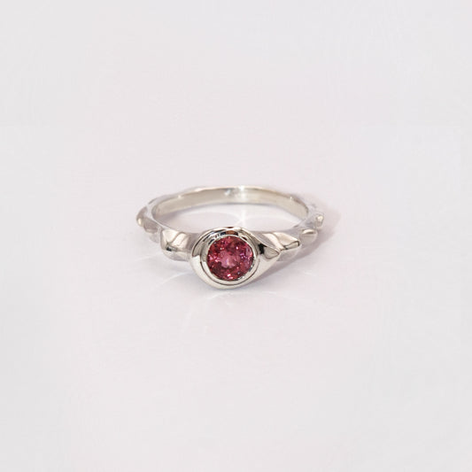 Silver ring with a pink gemstone on a light gray background