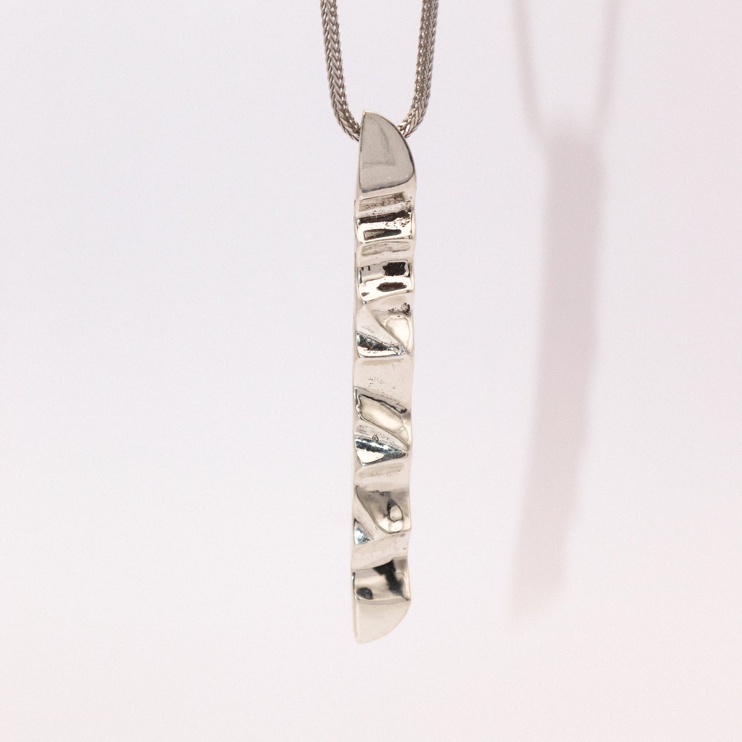 Silver necklace with a unique pendant on a light pink background