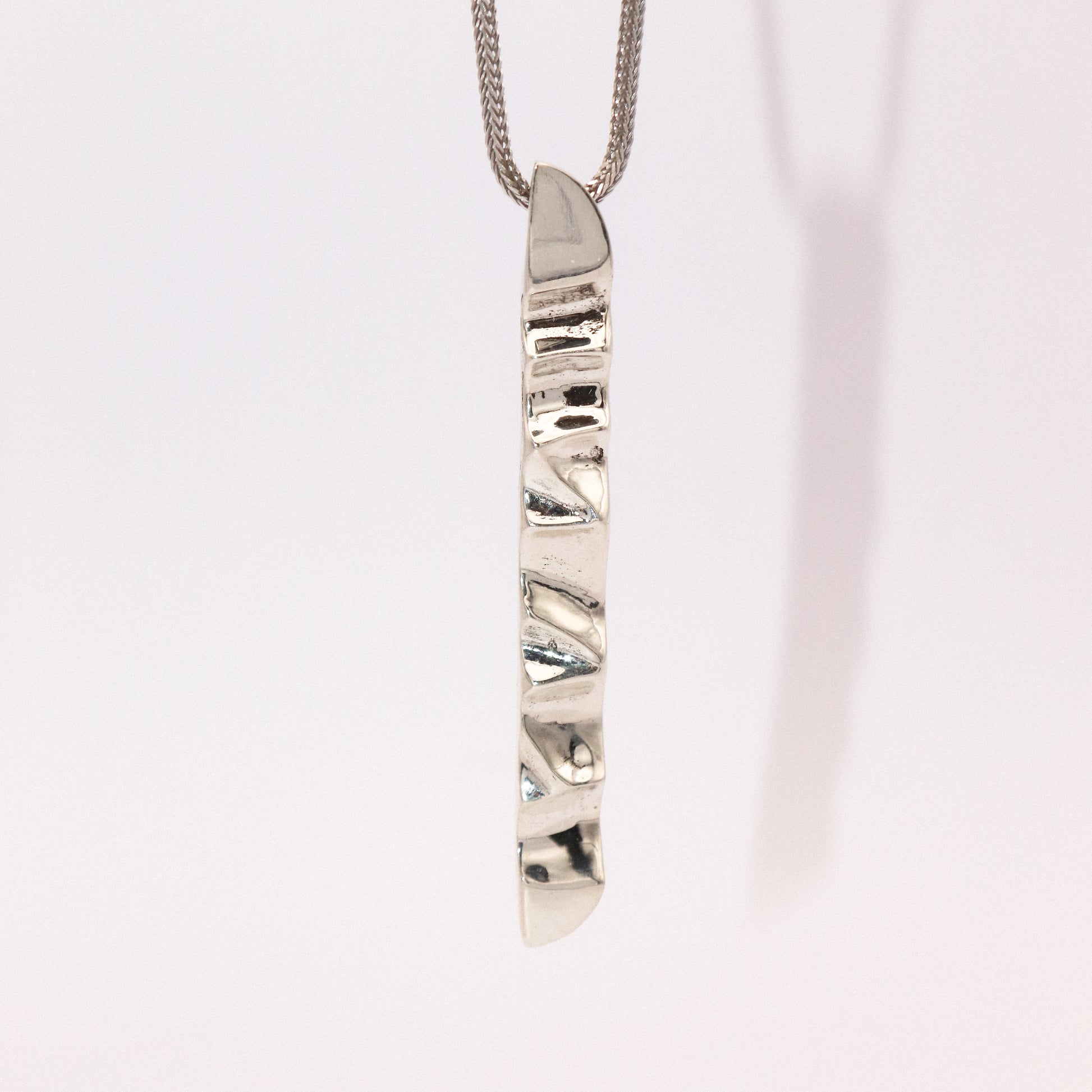 Silver necklace with a unique pendant on a light pink background