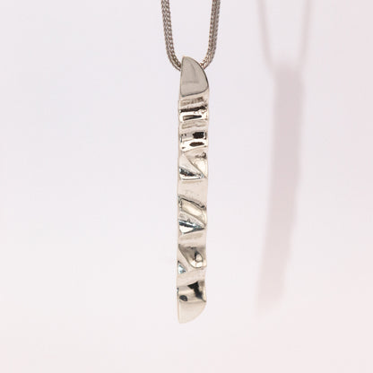 Silver necklace with a unique pendant on a light pink background