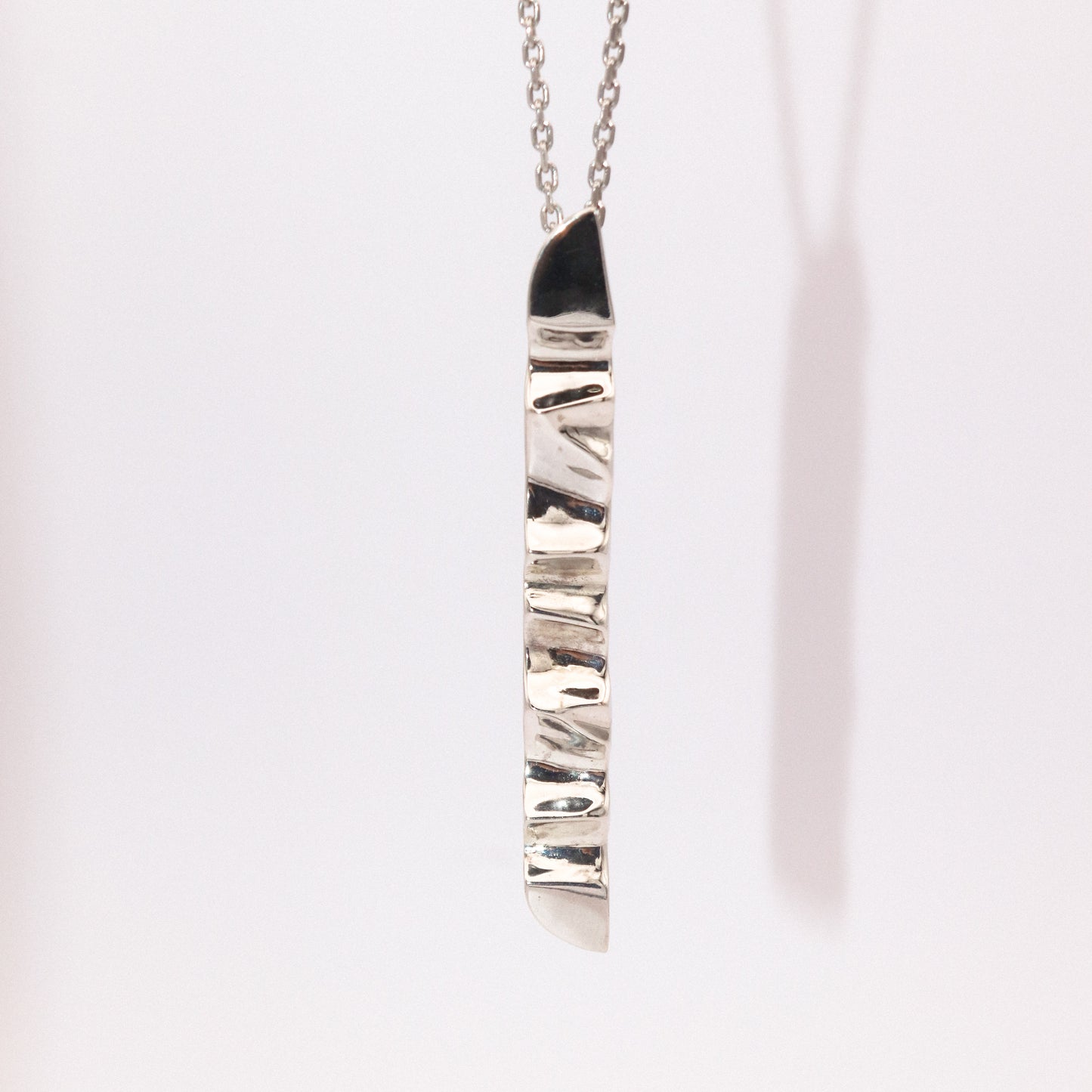 Silver necklace with a textured pendant on a light pink background