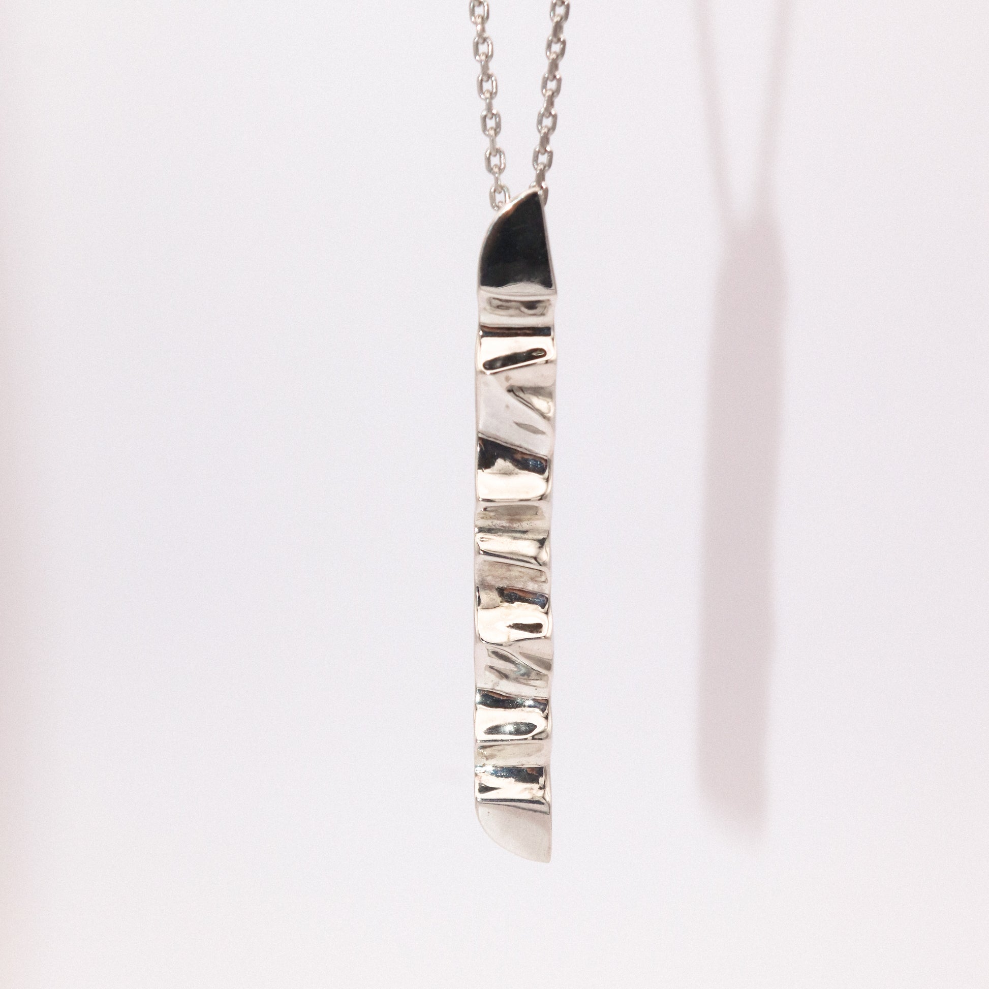 Silver necklace with a textured pendant on a light pink background