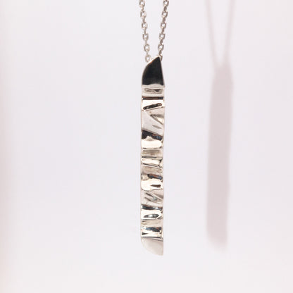 Silver necklace with a textured pendant on a light pink background