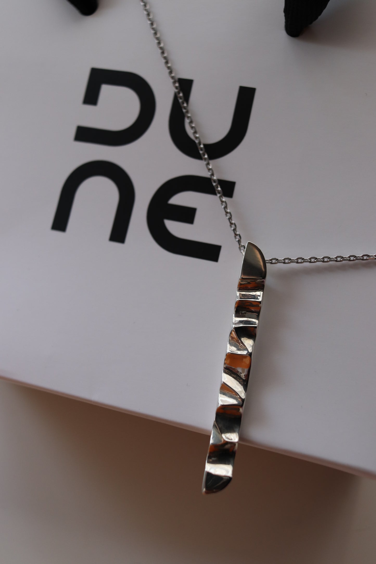 Silver necklace on a white card with black text