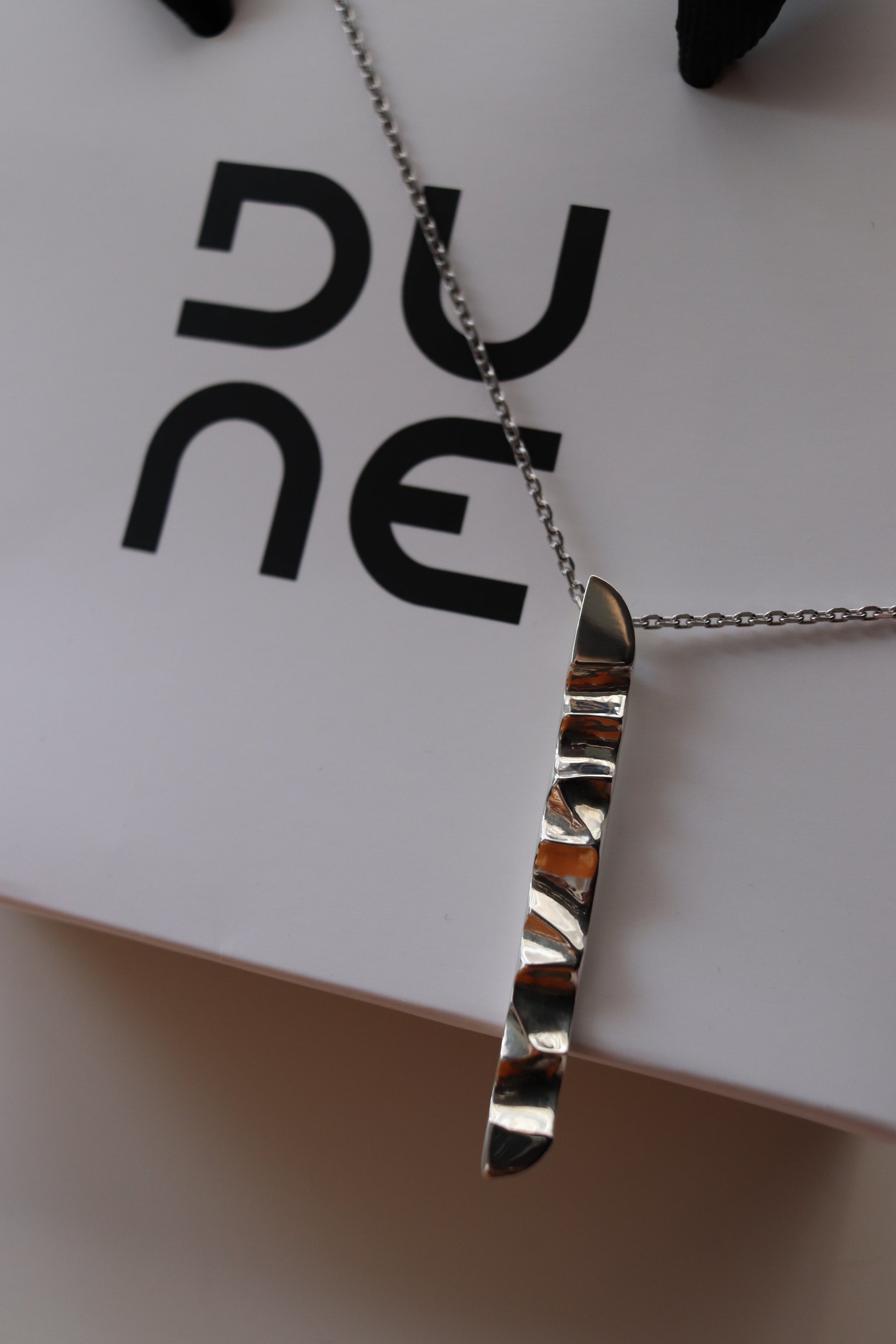 Silver necklace on a white card with black text