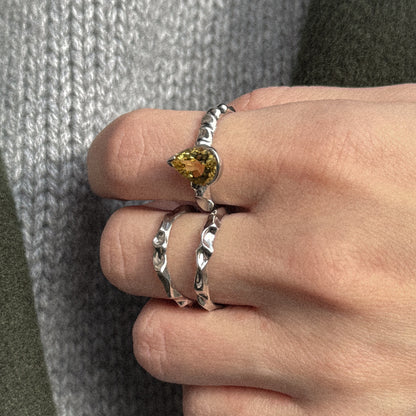 Close-up of a hand wearing two silver rings with gemstones against a textured fabric background.