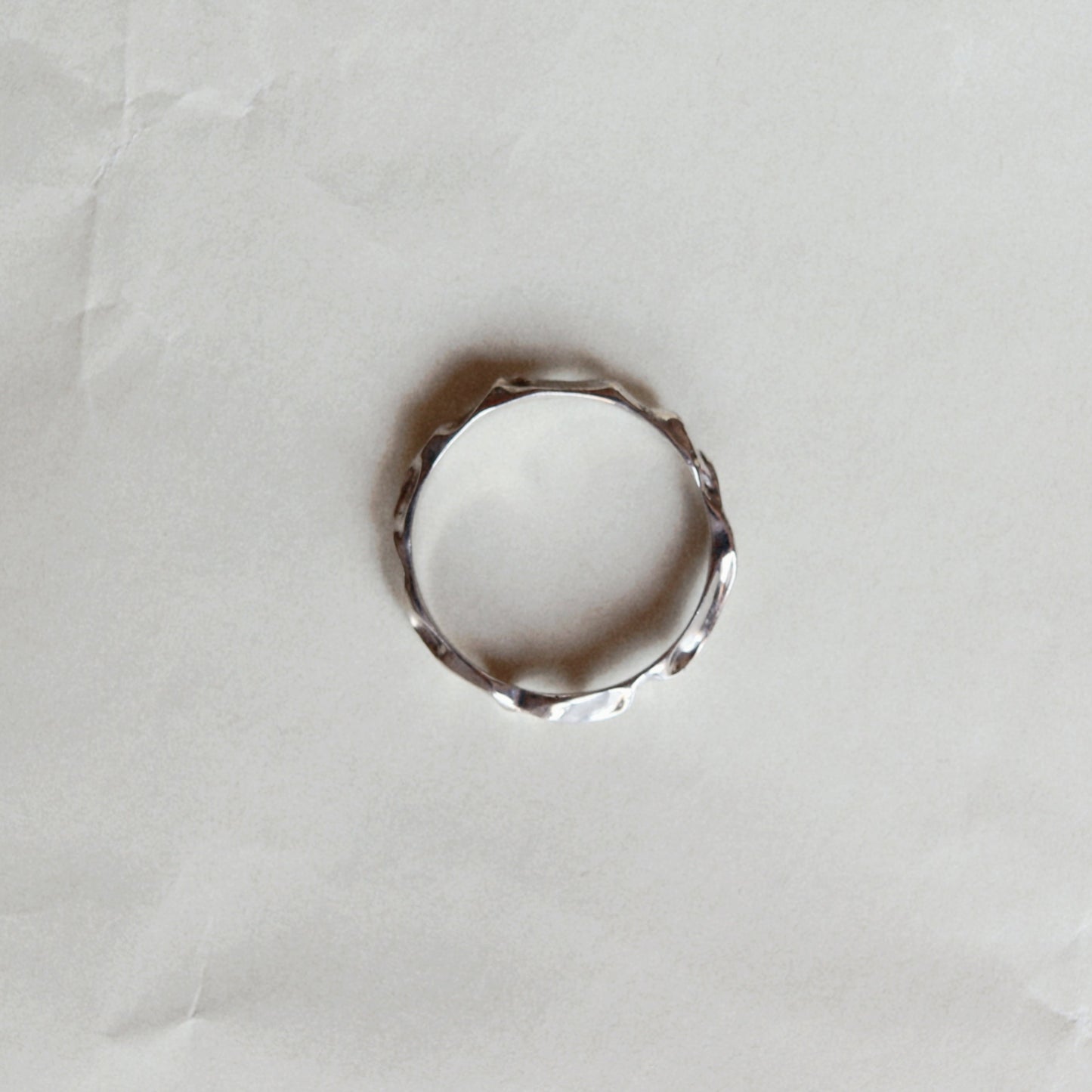 A thin silver-toned ring with a textured, organic wavy band, photographed on a wrinkled white paper background.