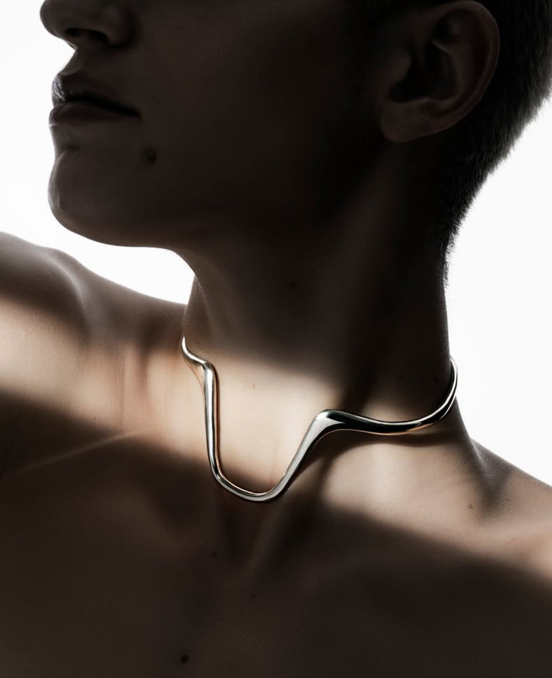 Close-up of a person wearing a modern silver necklace against a blurred background