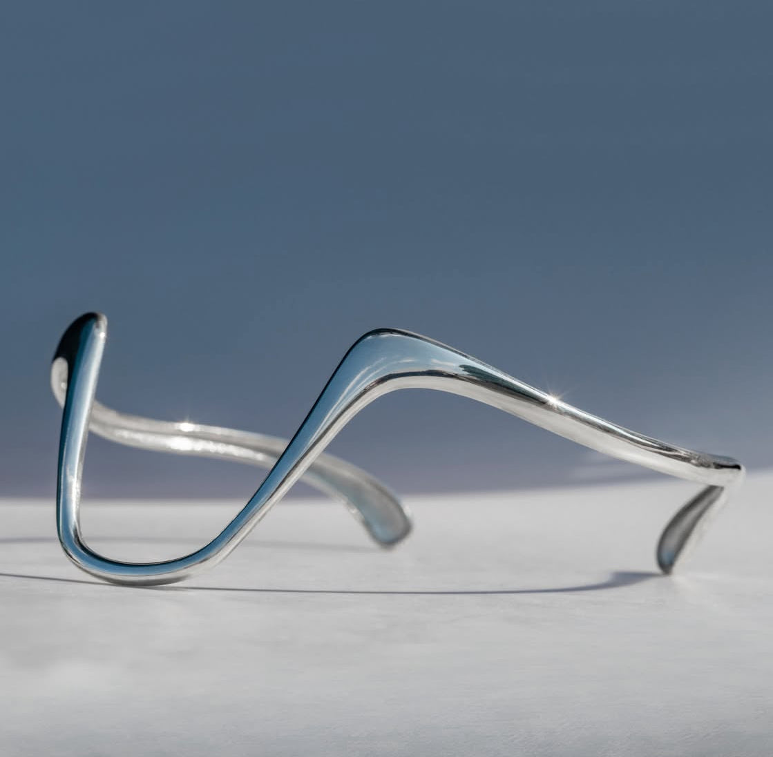 Silver bracelet on a light gray surface with a blue gradient background