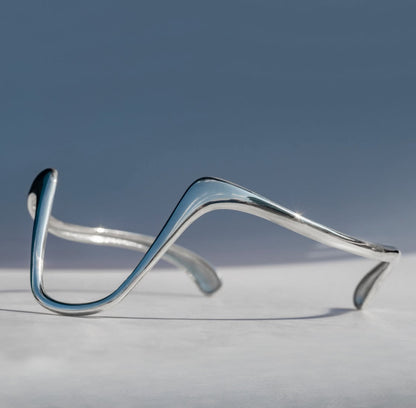 Silver bracelet on a light gray surface with a blue gradient background