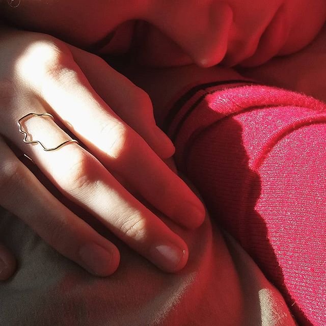 Close-up of a hand wearing a gold ring with a red background
