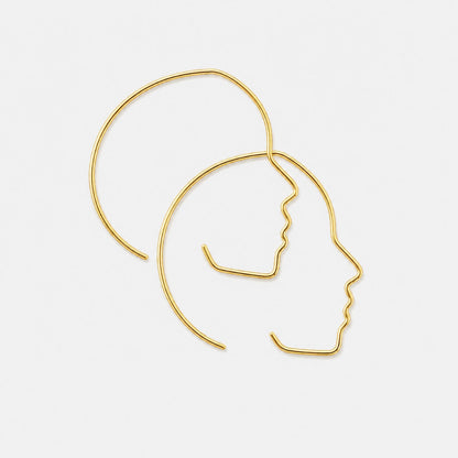 Gold profile-shaped earrings on a light gray background