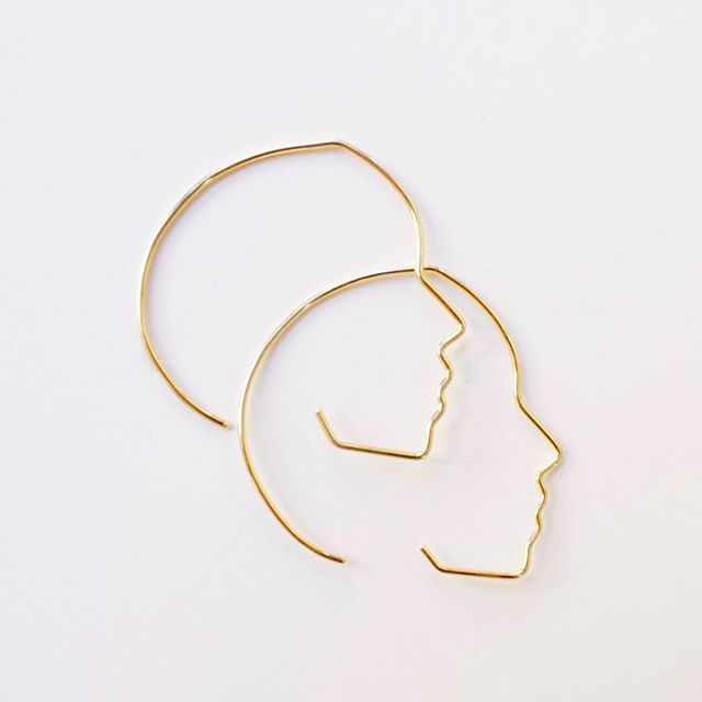 Gold hoop earrings with profile design on a white background