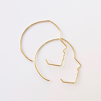 Gold hoop earrings with profile design on a white background