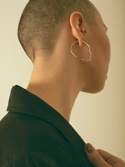 Person wearing a unique shaped earring against a neutral background