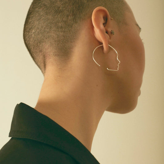 Person wearing a unique shaped earring against a neutral background
