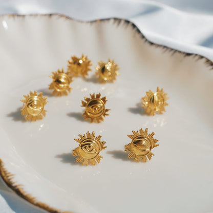 Gold sun-shaped earrings on a white ceramic dish with a white fabric background