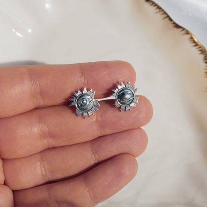 Silver earrings held between fingers against a white fabric background