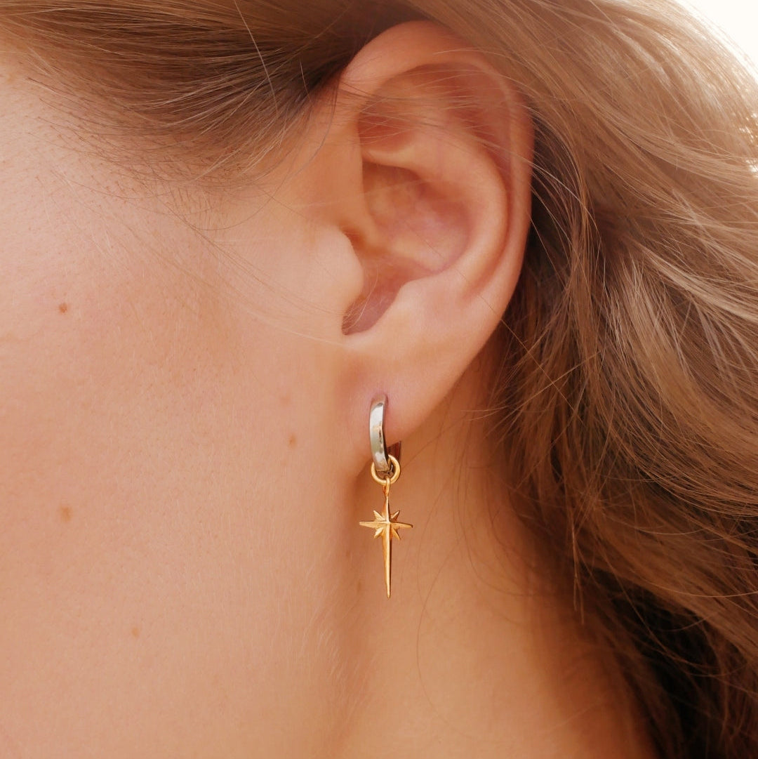 Gold hoop earring with a star detail worn by a person