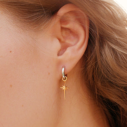 Gold hoop earring with a star detail worn by a person