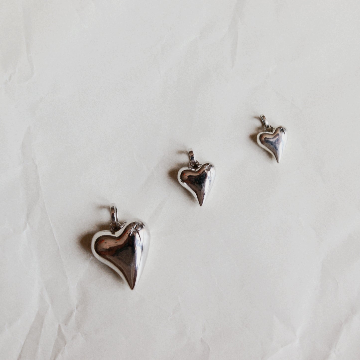Three small metallic heart-shaped charms or pendants arranged on a light beige textured paper background.