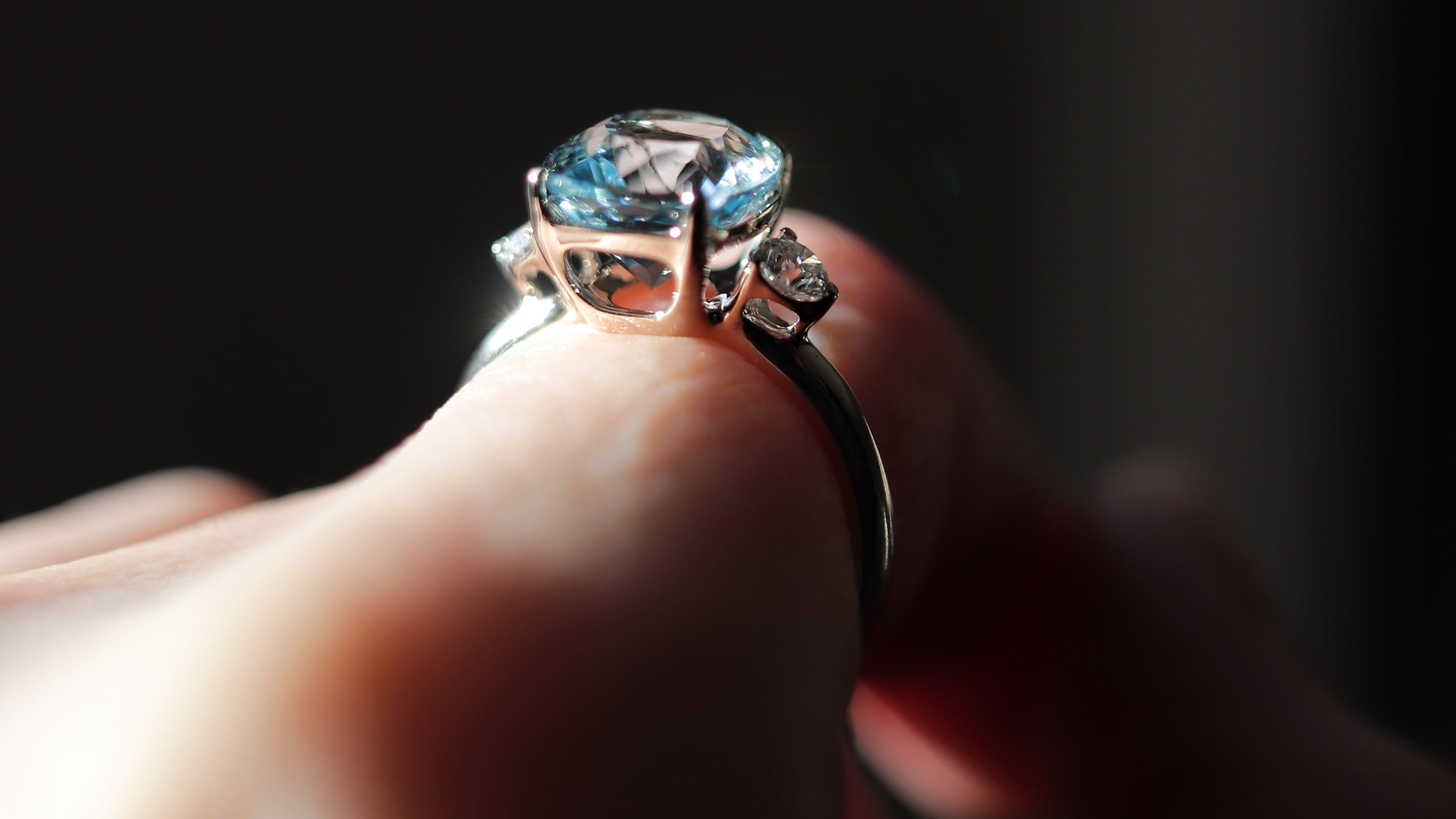 Close-up of a hand holding a ring with a blue gemstone against a dark background