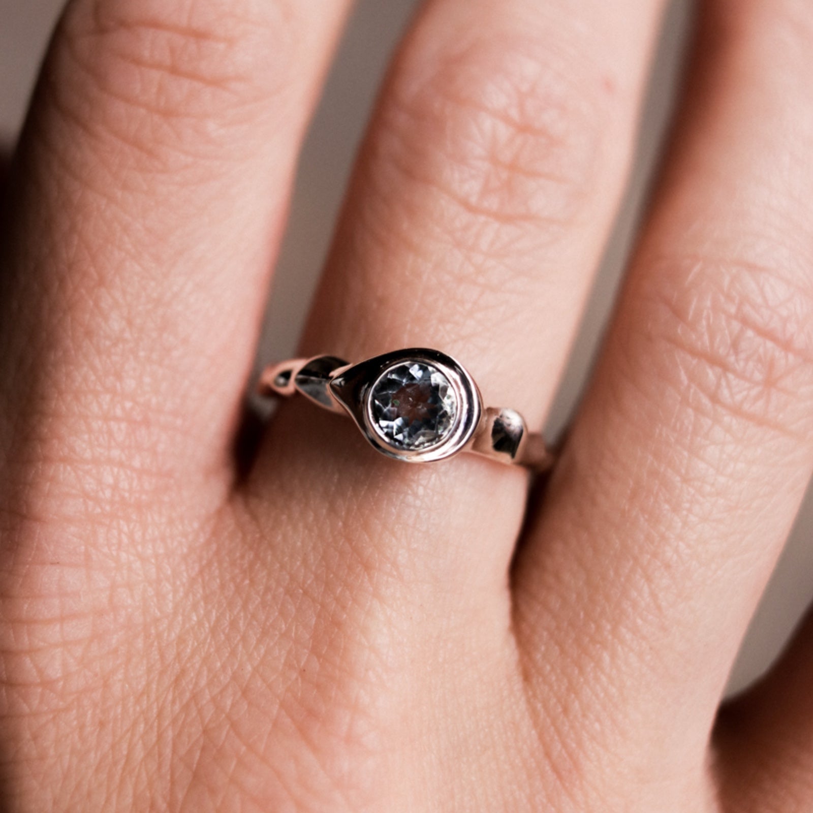 Rose gold ring with a central gemstone on a person's finger against a neutral background