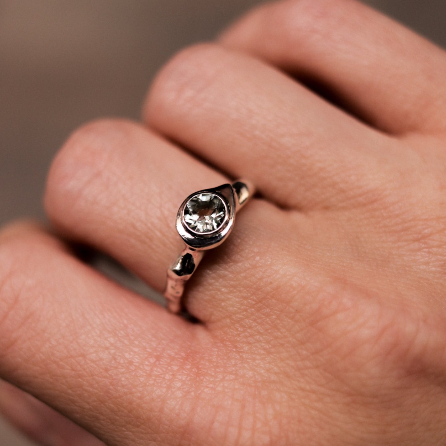 Rose gold ring with a diamond on a person's finger against a neutral background