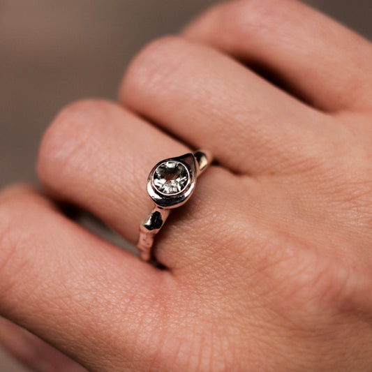 Rose gold ring with a diamond on a person's finger against a neutral background
