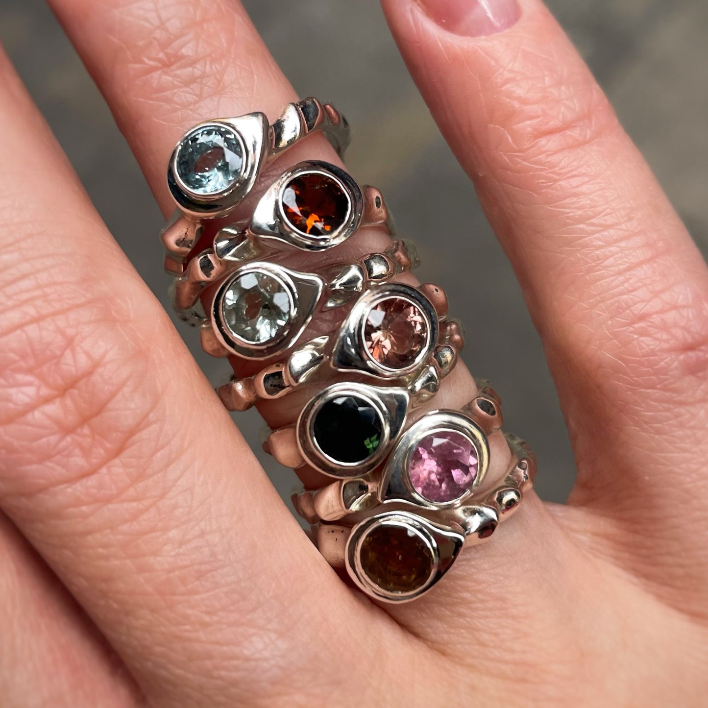 Ring with multicolored gemstones on a finger against a neutral background