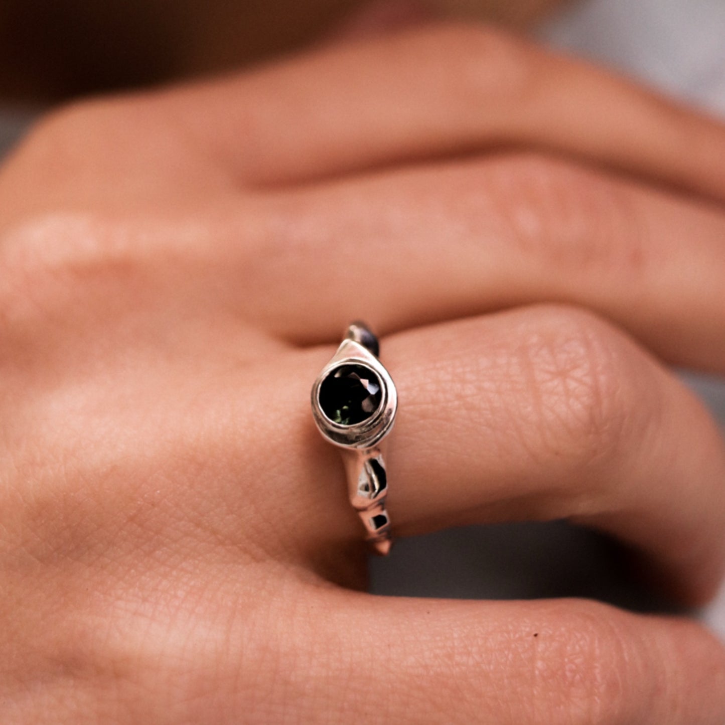 Silver ring with a black gemstone on a person's finger