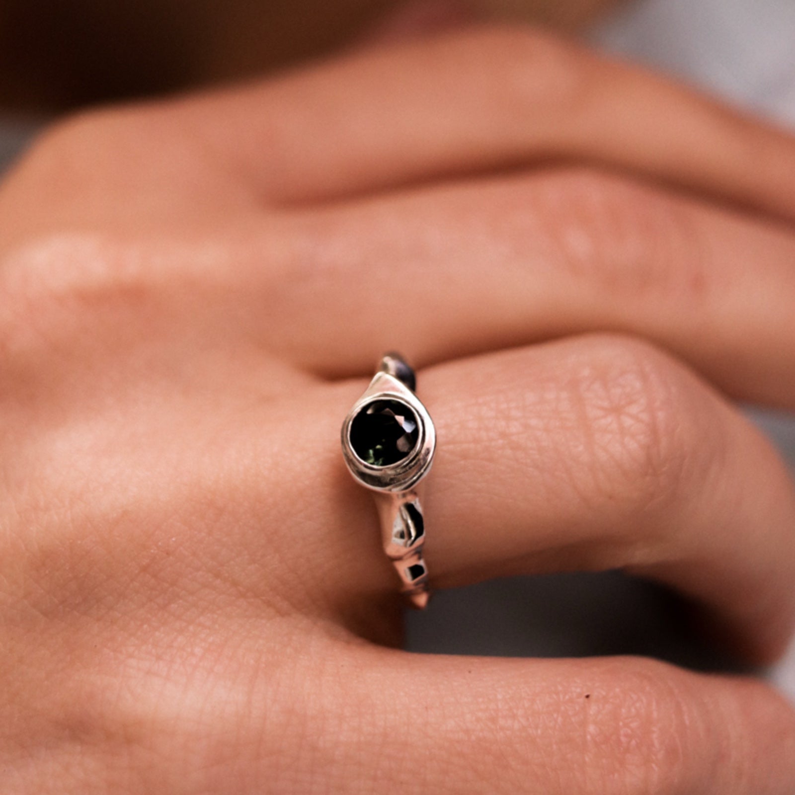 Silver ring with a black gemstone on a person's finger