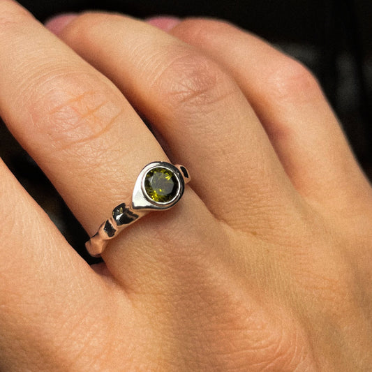 Close-up of a hand wearing a ring with a green gemstone.