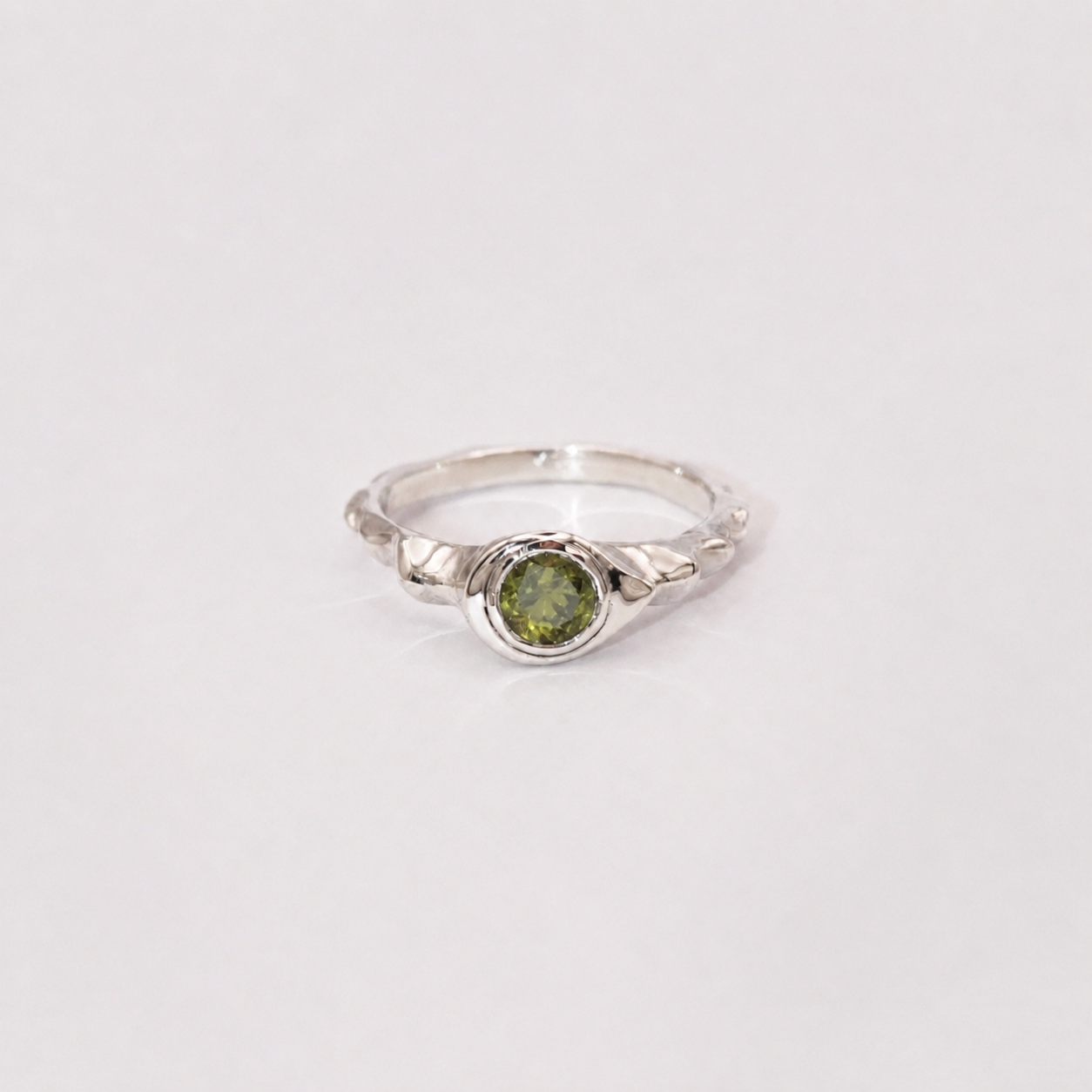 Silver ring with a green gemstone on a light gray background