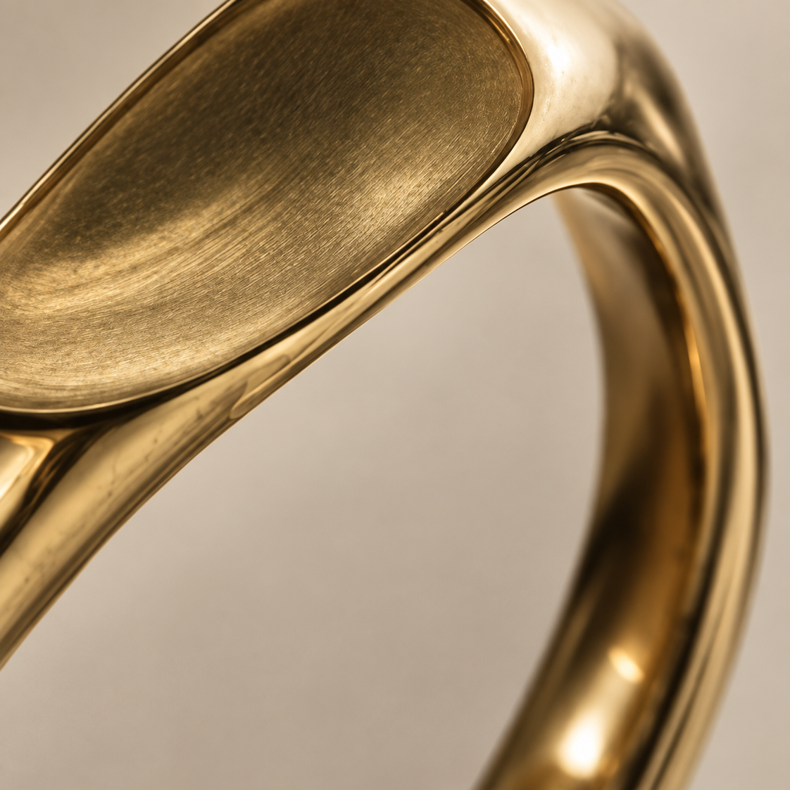 Close-up of a polished yellow gold signet ring with a brushed and satin finish, set against a neutral light gray background.